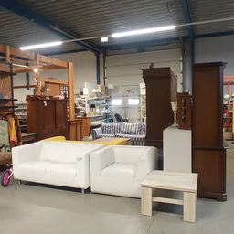 Witte zithoek met bank en fauteuils naast houten kasten en meubels in kringloopwinkel