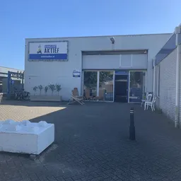 Voorgevel van kringloopwinkel met ingang, wit blok op voorplein en fietsen ernaast