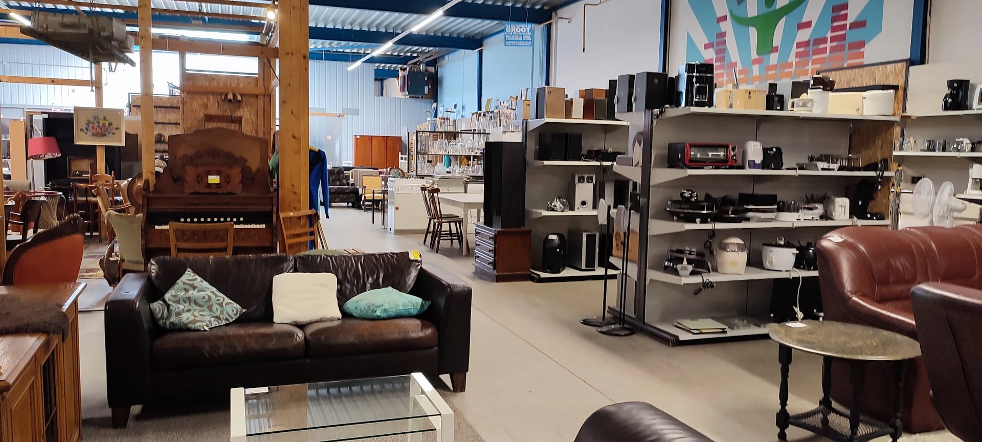Winkelvloer met bruine leren bank, zwarte kasten met huishoudelijke apparaten en meubels in een kringloopwinkel