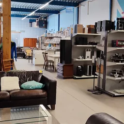 Winkelvloer met bruine leren bank, zwarte kasten met huishoudelijke apparaten en meubels in een kringloopwinkel