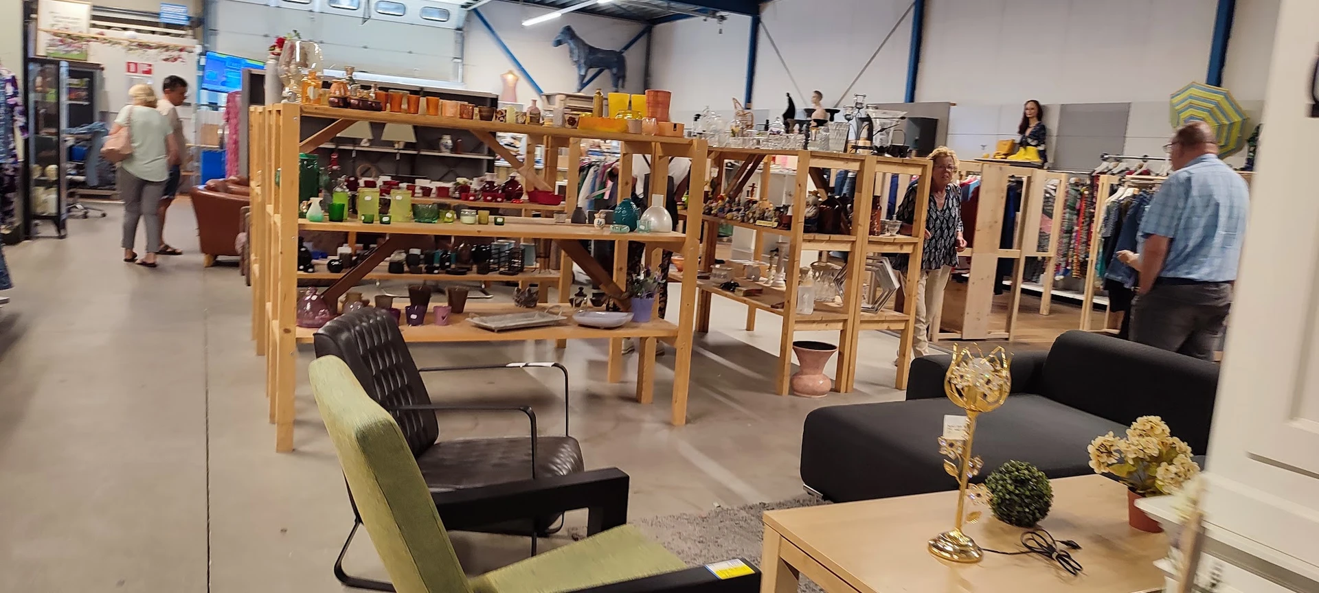 Binnenzicht van kringloopwinkel met houten stellingen, meubels en uitgestalde spullen op meerdere niveaus