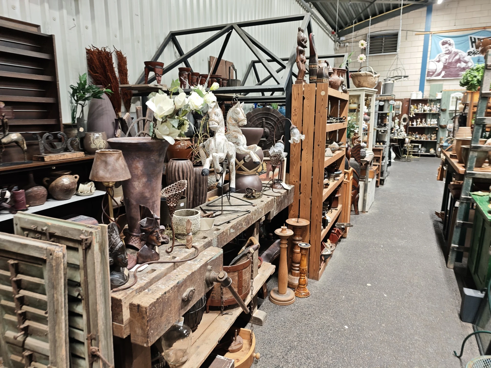 Uitgestalde decoratieve spullen, meubels en accessoires in een kringloopwinkel, waaronder lampen, vazen, bloemen en houten it