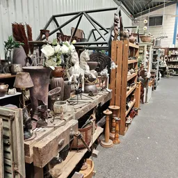 Uitgestalde decoratieve spullen, meubels en accessoires in een kringloopwinkel, waaronder lampen, vazen, bloemen en houten it