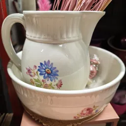 Witte porseleinen schenkkan met blauwe en roze bloemen op onderschotel