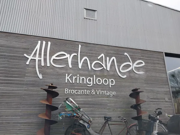 Gevel van kringloopwinkel met wit logo 'Allerhande Kringloop' en ondertitel 'Brocante & Vintage', met daaronder enkele fietse