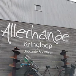 Gevel van kringloopwinkel met wit logo 'Allerhande Kringloop' en ondertitel 'Brocante & Vintage', met daaronder enkele fietse