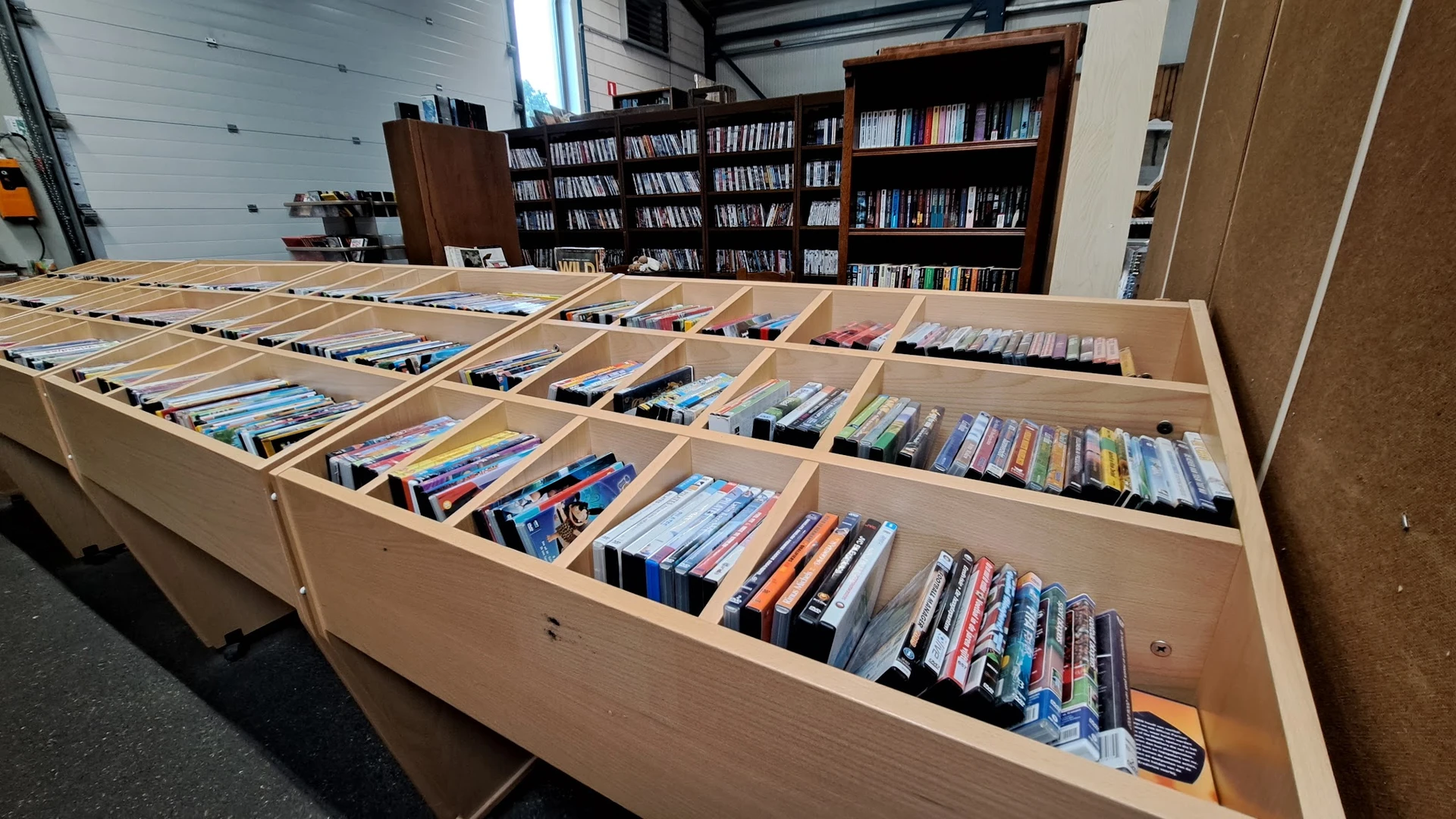 Houten sorteerkast met veel vakken gevuld met DVD's en blu-rays, op de achtergrond boekenkastjes