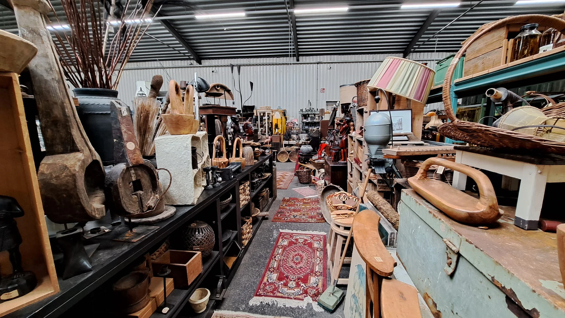 Binnenaanzicht van kringloopwinkel met diverse gebruikte meubels, huishoudartikelen en spullen langs gangpad met rood tapijt