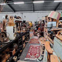Binnenaanzicht van kringloopwinkel met diverse gebruikte meubels, huishoudartikelen en spullen langs gangpad met rood tapijt