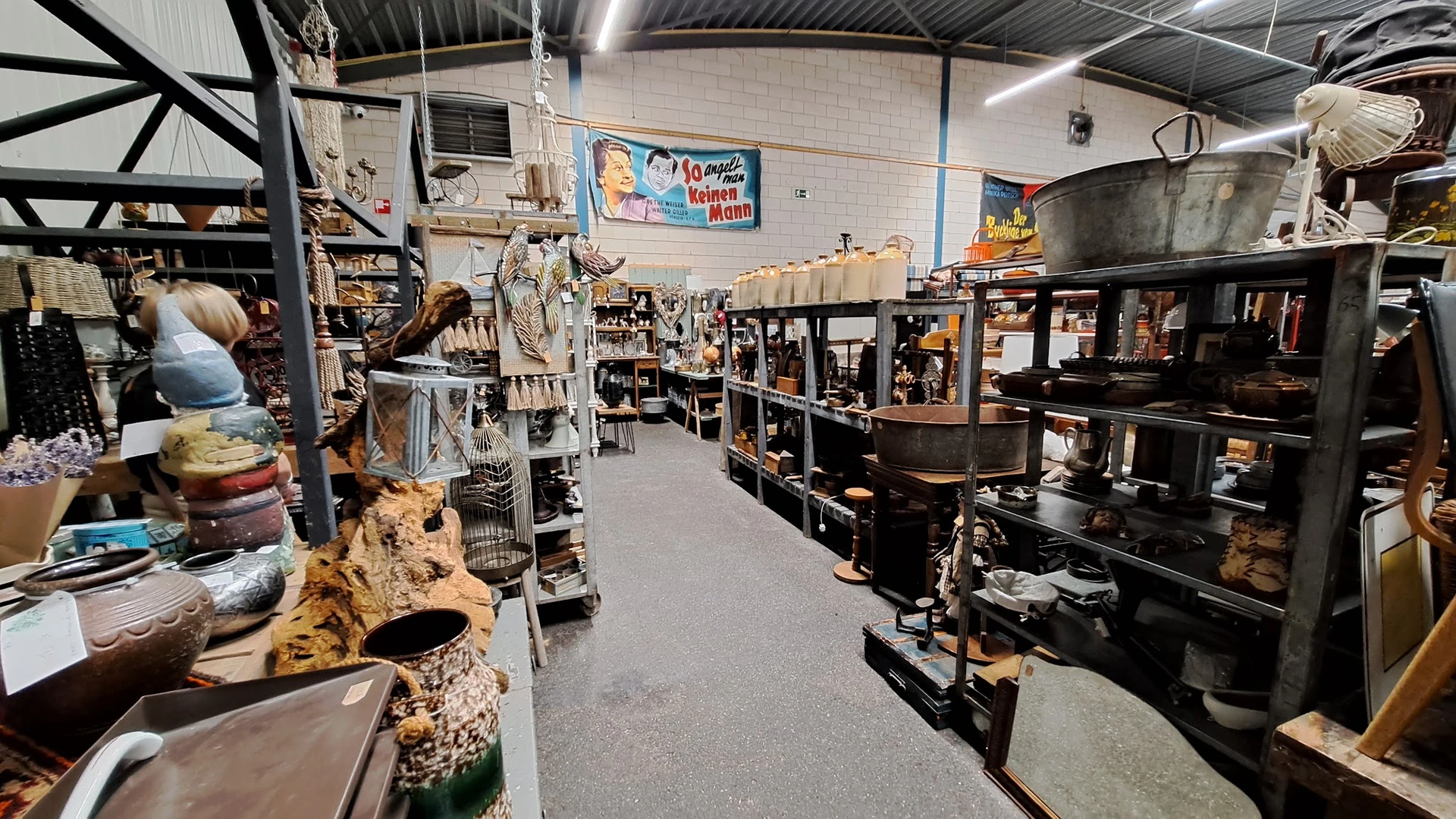 Winkelvloer met stellingen vol huishoudelijke spullen, meubels en gebruikte goederen in een kringloopwinkel
