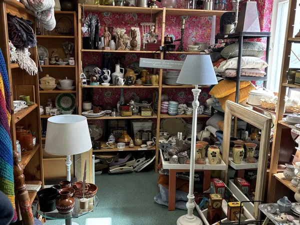 Overzicht van kringloopwinkel met houten kasten, diverse huishoudelijke spullen, lampen en decoratie