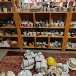 Houten stellingen gevuld met verzameling serviesgoed en mokken in verschillende kleuren en designs