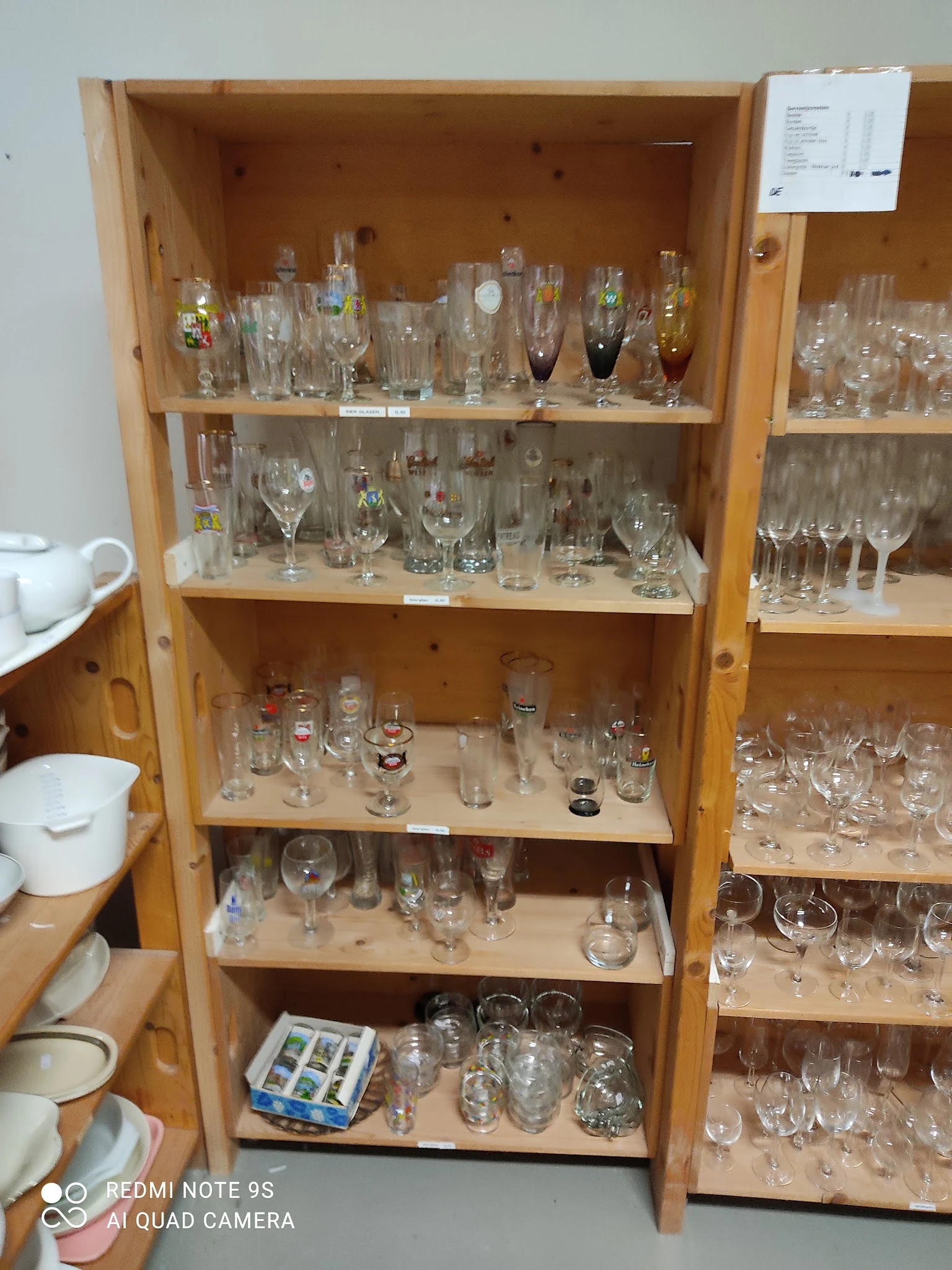 Houten vitrinekast met meerdere schappen vol verschillende glazen, bekers en drinkglazen