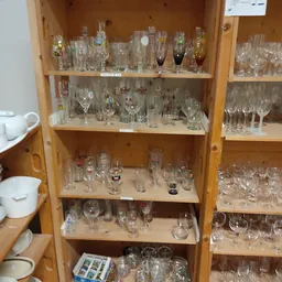 Houten vitrinekast met meerdere schappen vol verschillende glazen, bekers en drinkglazen