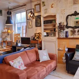Huiskamer-achtige winkelruimte met roze bank, bureauhoek, wandkasten met decoratie en vintage meubels