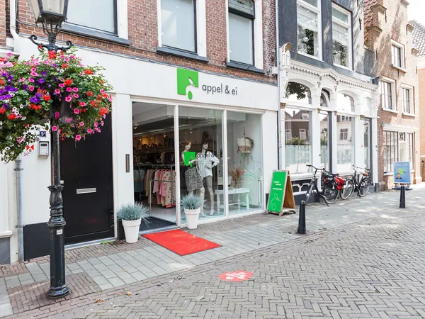 Winkelgevel van kringloopwinkel Appel & Ei met witte pui, groene accenten en bloemenhangende mand