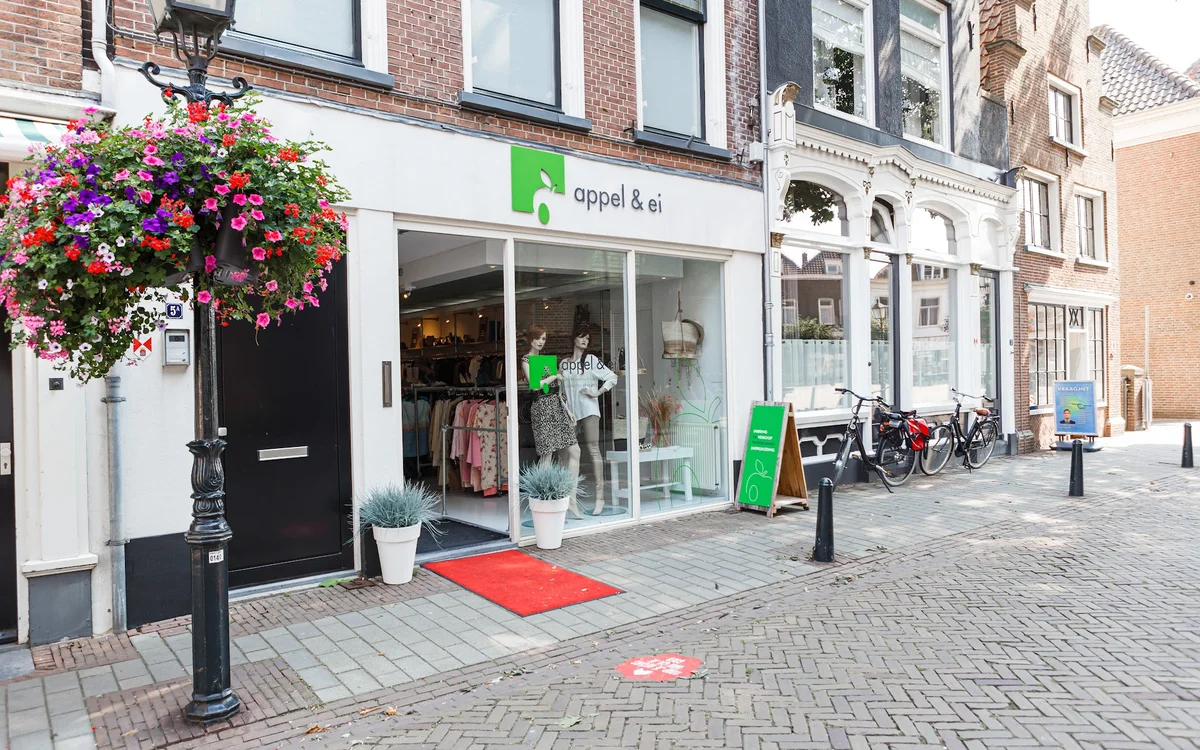 Winkelgevel van kringloopwinkel Appel & Ei met witte pui, groene accenten en bloemenhangende mand
