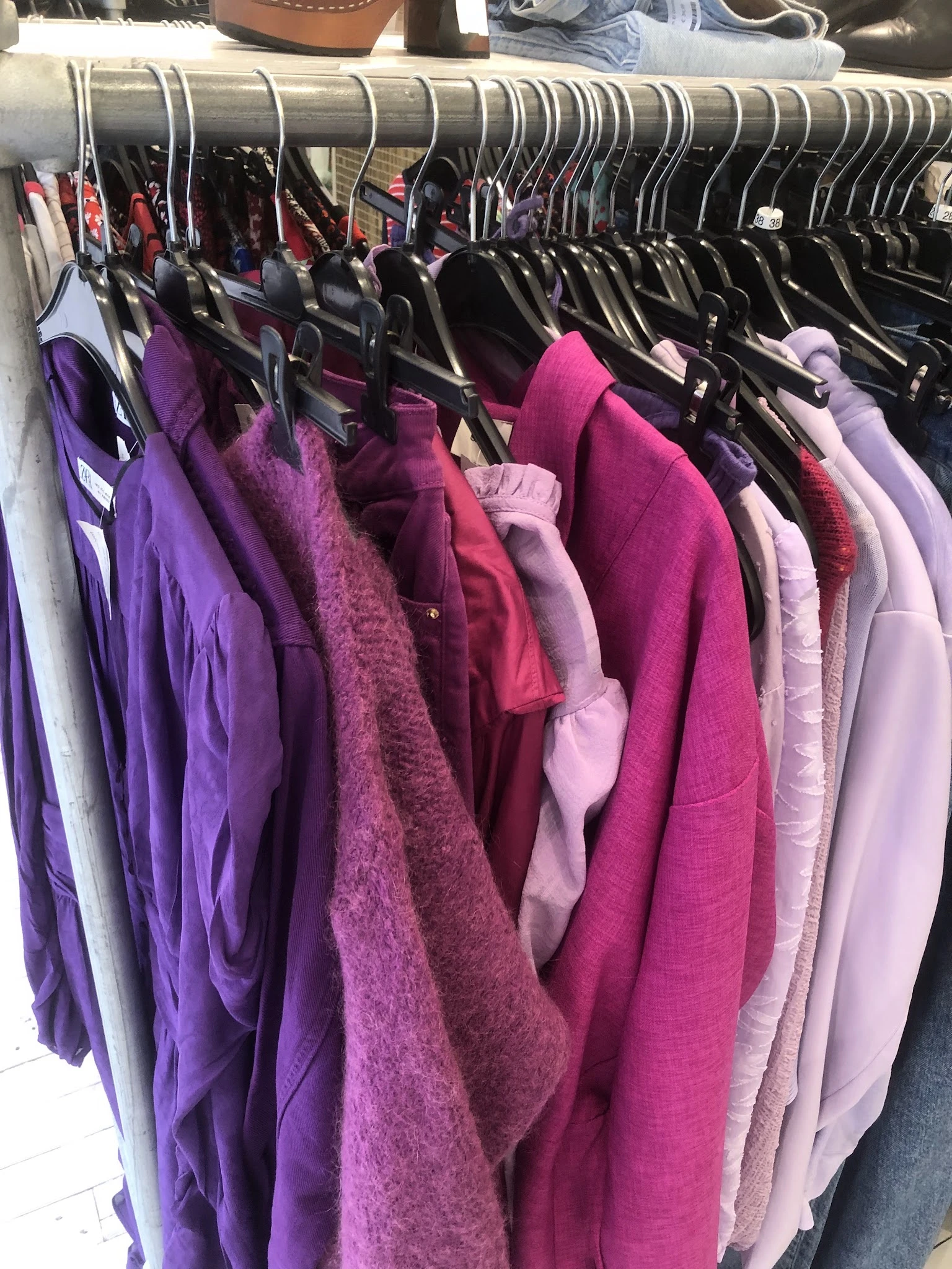 Rekken met tweedehands dameskledij in paarse en roze tinten op hangers