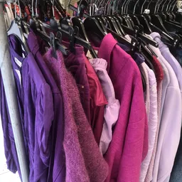Rekken met tweedehands dameskledij in paarse en roze tinten op hangers