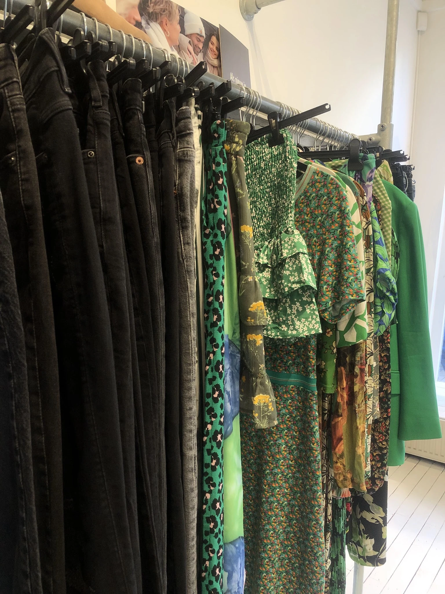 Rekken met tweedehands kleding, voornamelijk jurken en blouses in zwart, groen en gemengde patronen