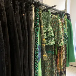Rekken met tweedehands kleding, voornamelijk jurken en blouses in zwart, groen en gemengde patronen