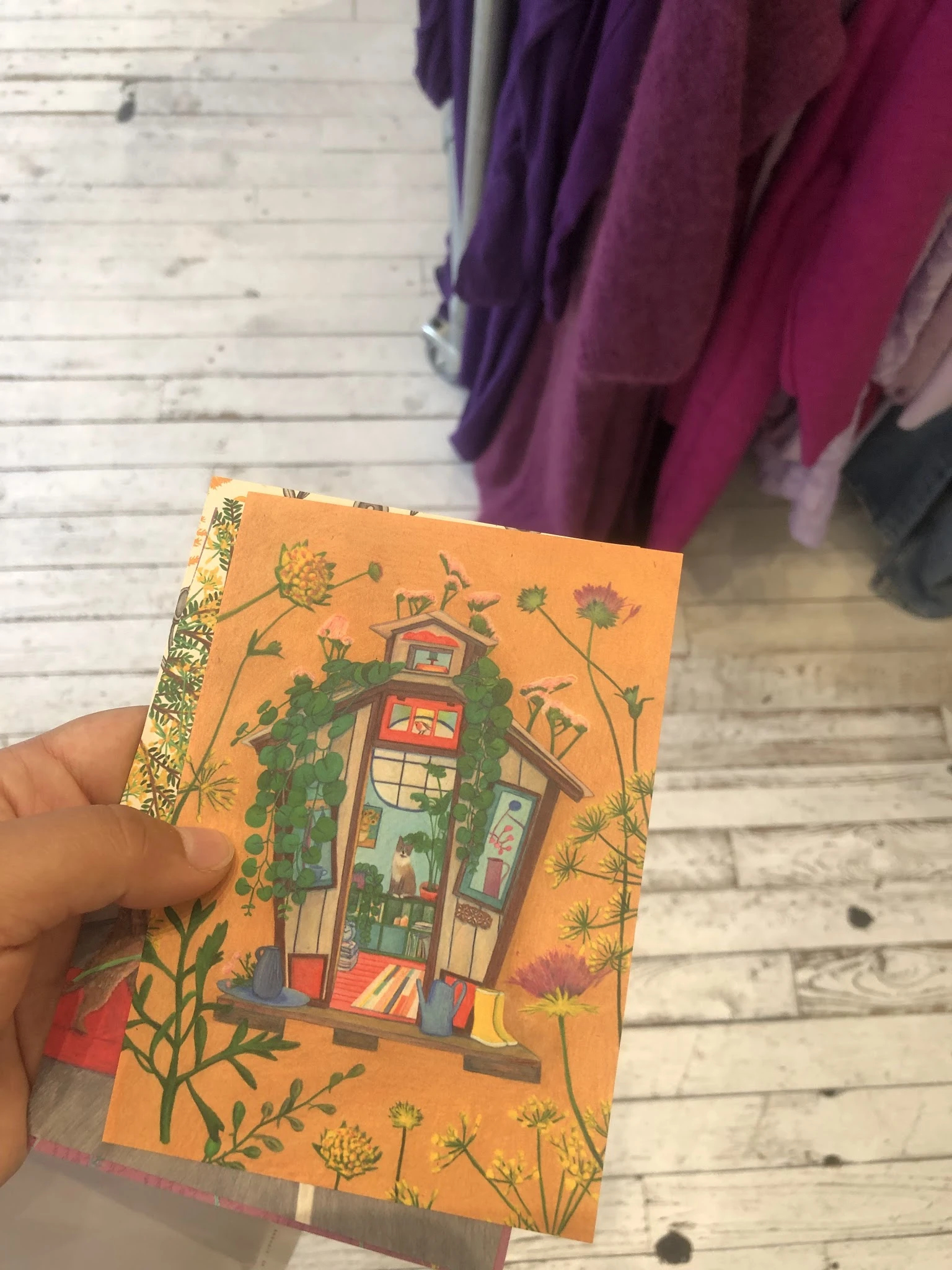 Boek met oranje kaft met illustratie van een huis omgeven door bloemen, gouden decoratieve rand