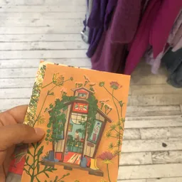 Boek met oranje kaft met illustratie van een huis omgeven door bloemen, gouden decoratieve rand
