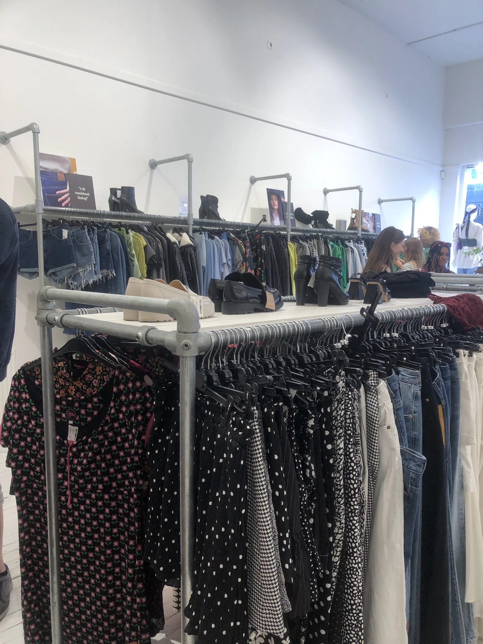 Rekken met tweedehands kleding in verschillende kleuren en patronen, waaronder zwarte en bedrukte items