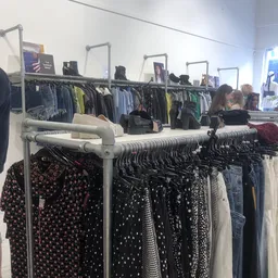 Rekken met tweedehands kleding in verschillende kleuren en patronen, waaronder zwarte en bedrukte items
