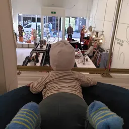 Mannequin met gestreepte trui en grijze broek voor winkelraam met kledingrekken en uitgeklede poppen op achtergrond