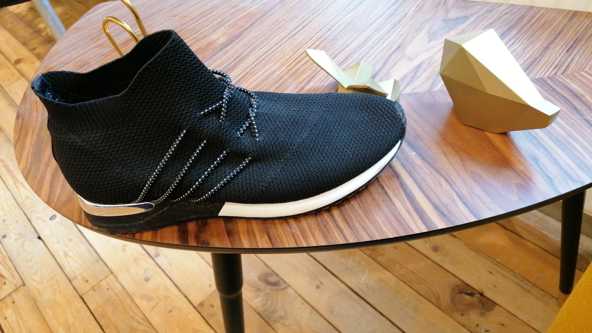 Zwarte sneaker met witte zool op glazen tafel, naast kartonne doos