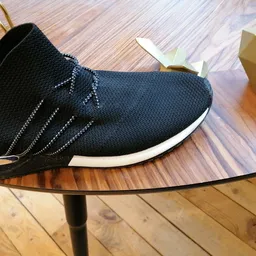 Zwarte sneaker met witte zool op glazen tafel, naast kartonne doos