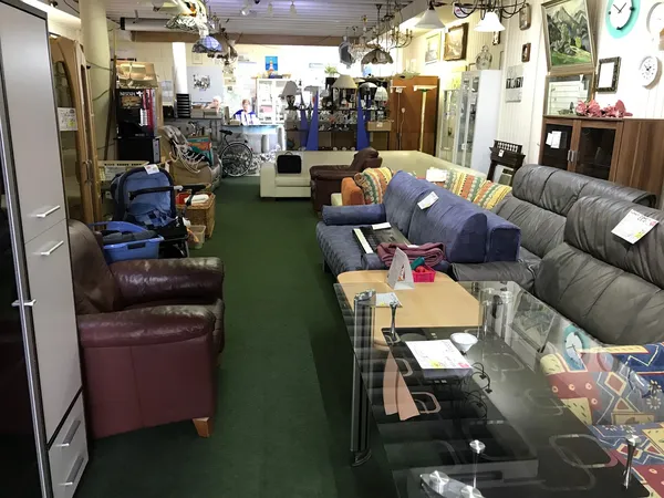 Winkelinterieur met grijze banken, bruine fauteuil, houten meubels en diverse artikelen op groene vloer