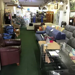 Winkelinterieur met grijze banken, bruine fauteuil, houten meubels en diverse artikelen op groene vloer