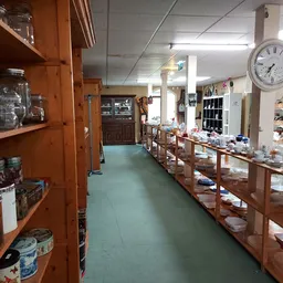 Binnenzicht kringloopwinkel met houten stellingen vol servies en huishoudartikelen, groen linoleum vloer, plafondverlichting 