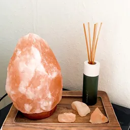 Himalayazoutsteen lamp, geurstokjes in fles en decoratieve stenen op houten oppervlak