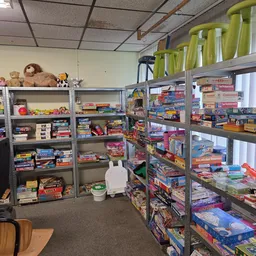 Winkelinterieur met stellingen vol boeken, spellen en speelgoed; groene plastic containers op bovenkast
