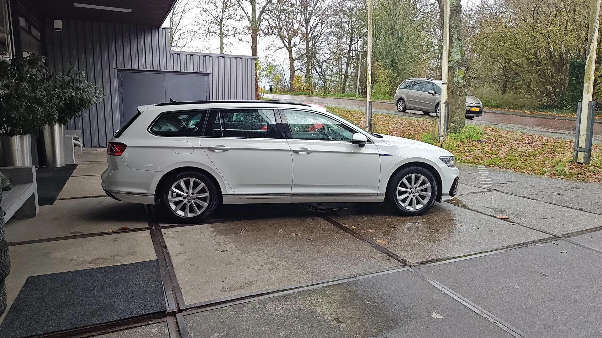 Witte stationcar (wagon) geparkeerd op bedrijfsterrein met loods en bomen op achtergrond