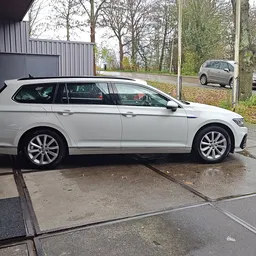 Witte stationcar (wagon) geparkeerd op bedrijfsterrein met loods en bomen op achtergrond