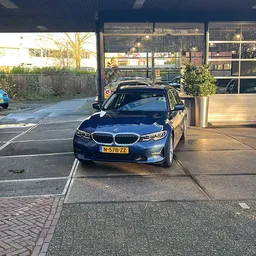 Blauwe BMW-auto geparkeerd voor de gevel van autobedrijf Heijne