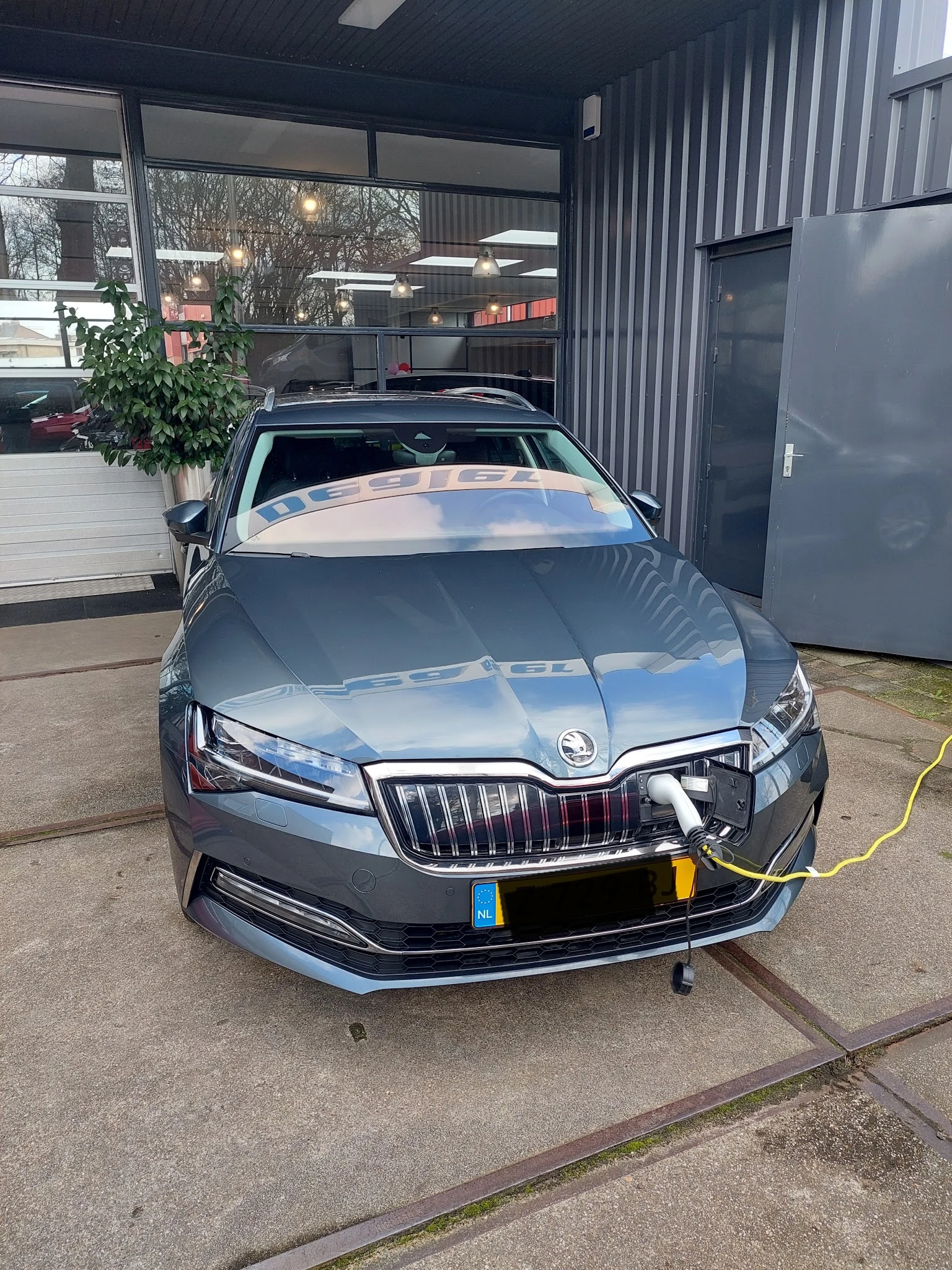 Grijze Skoda auto van voren gefotografeerd op het bedrijfsterrein, met laadkabel aangesloten