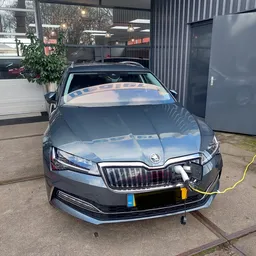 Grijze Skoda auto van voren gefotografeerd op het bedrijfsterrein, met laadkabel aangesloten