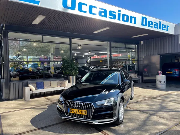 Voorkant van autobedrijf met zwarte Audi-auto op parkeerplaats en winkelname boven de glazen puien