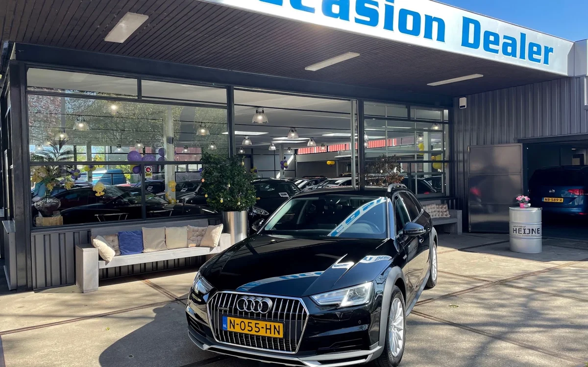 Voorkant van autobedrijf met zwarte Audi-auto op parkeerplaats en winkelname boven de glazen puien