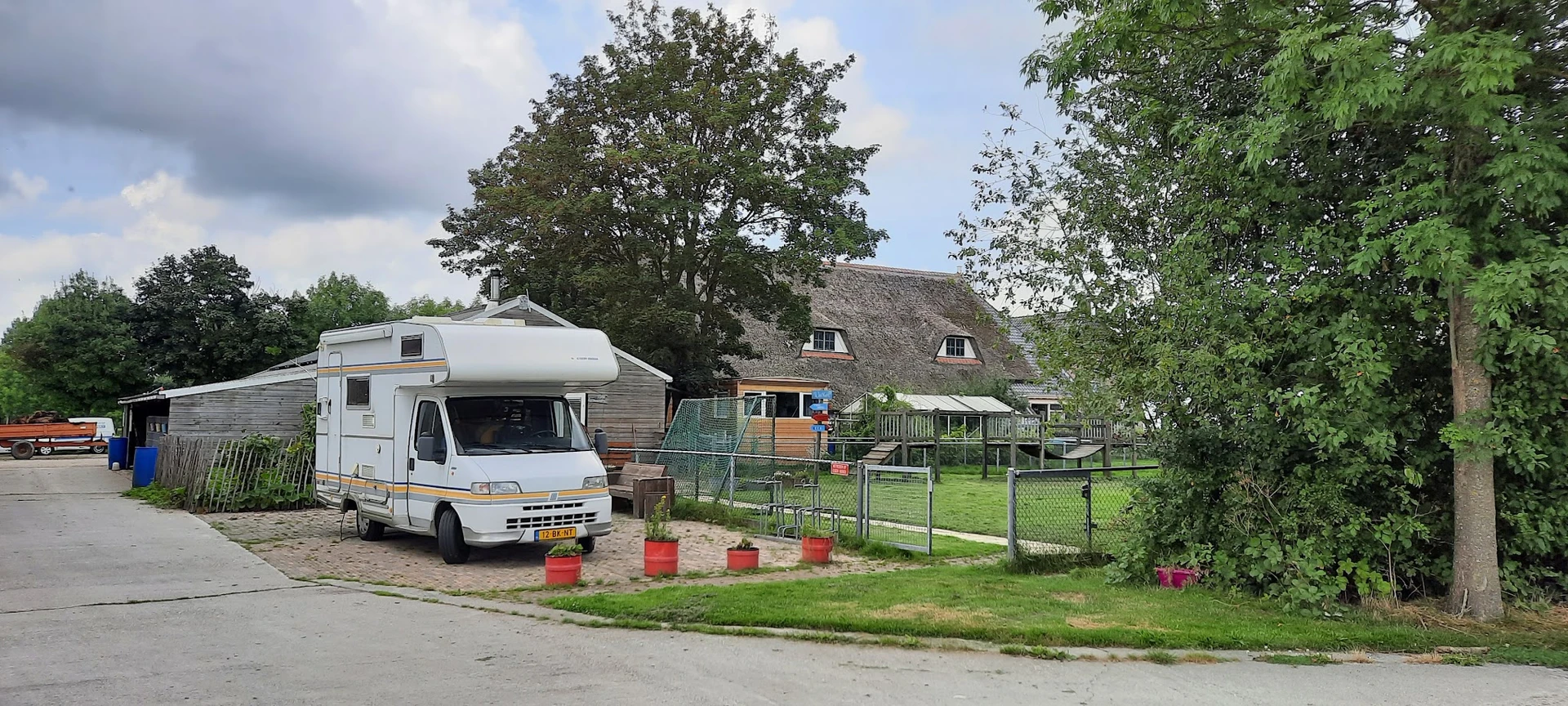 Witte camper geparkeerd voor boerderij met rieten dak en groene omheining