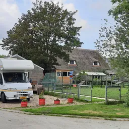 Witte camper geparkeerd voor boerderij met rieten dak en groene omheining