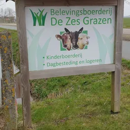 Informatiebord van De Zes Grazen met logo en tekst over kinderboerderij en dagbesteding