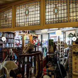Winkelvloer met boekenrekken, muziekinstrumenten, meubels en diverse tweedehandsartikelen onder glazen kastdeuren