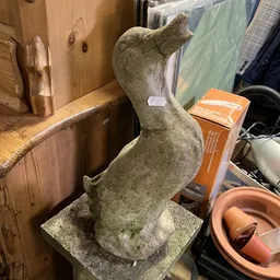 Stenen tuinbeeld van een zittende figuur tussen diverse winkelspullen