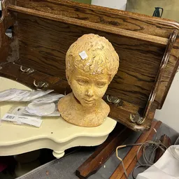 Goudkleurig buste van een jongen of jong gezicht op een witte voet, staande op een kastje